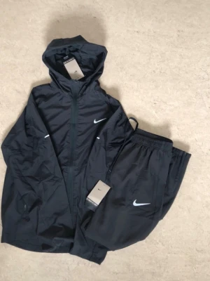 Svart träningsset från Nike - Snyggt svart träningsset från Nike med jacka och byxor. Settet är för litet på mig därav då jag säljer , använt 5-10 gånger som ny 🆕 