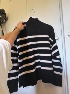 Svartvit randig stickad polotröja - Säljer en svart stickad tröja med vita horisontella ränder och hög polokrage. Tröjan har långa ärmar och ribbade muddar samt en avslappnad passform. Från zara och tyvärr knappt andvänd 