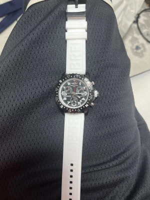 Breitling Endurance Pro vit klocka - Snygg Breitling Endurance Pro klocka med vit silikonrem och svart urtavla. Klockan har flera funktioner, tydliga vita siffror och detaljer i rött. Boetten är svart och remmen har Breitling-loggan präglad. Perfekt för dig som gillar sportig och modern stil.