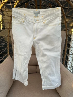 Vita jeans från H&M Dubster - Snygga vita caprijeans från H&M Dubster med gulaktiga sömmar, eldliknande broderier på bakfickorna och dragkedja vid benslut. 