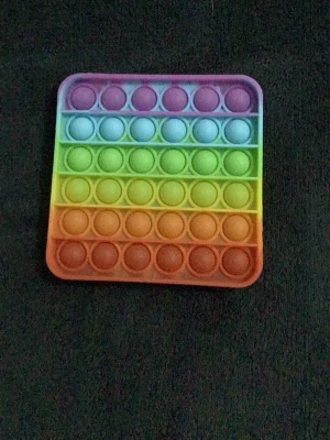 Fidget pop it i regnbågsfärger - Säljer en fyrkantig pop it i regnbågsfärger. Den är gjord av mjukt silikon och har flera rader med bubblor att trycka på. Perfekt för att sysselsätta händerna eller stressa ner.
