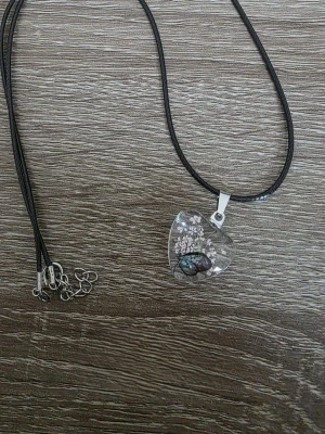Halsband med hjärthänge och blommor - Unikt halsband med svart snöre och ett genomskinligt hjärthänge fyllt med små ljus rosa blommor samt en fjäril. Hänget har en metallögla och ger en romantisk och bohemisk känsla. Perfekt accessoar för att lyfta din stil.