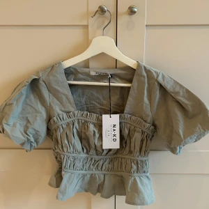 Grön blus med volang  - Såå söt oanvänd grön blus från NA-KD med puffiga korta ärmar och volangdetaljer. Blusen är lite croppad o har en v-ringad design. Den är tillverkad i ett lätt material som ger en luftig känsla. Aldrig använd- då den är för liten (därför finns det inga bilder med den på). 