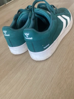 Gröna Hummel sneakers med vit sula - Om ni är intresserade kan ni föreslå nytt pris måste inte vara just 300,använda Max 3 gånger, Snygga gröna sneakers från Hummel med klassiska vita pilar på sidan och vit sula. Skorna har lågt skaft, gröna skosnören och är tillverkade i textil och syntetmaterial. Perfekta för dig som vill ha en sportig och stilren look.