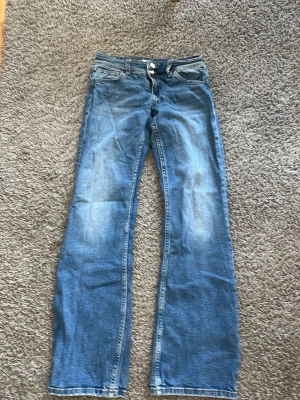 Blåa utsvängda jeans - Säljer ett par blåa jeans med utsvängda ben och ljusa slitningar framtill. Klassisk femficksmodell i mjukt denimtyg. Perfekta för dig som gillar retrostil och vill ha ett par riktigt sköna jeans med bred passform.