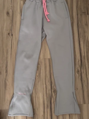 Syna world track byxor - Gråa syna world tracksuit byxor med rosa snören och mönster. Storlek small men passar som M