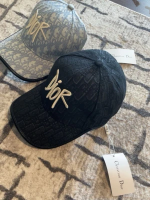 Svart Dior keps med broderad logga - Säljer två stycken Dior keps för 600kr. Första är svart med gul färg med logan dior. Och den andra blå färgad med gul färg på logan. 