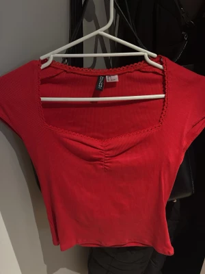 Röd ribbad topp med v-ringning - Snygg röd ribbad topp med v-ringad hals och dekorativ kant. Toppen har korta ärmar och lätt rynkning vid bysten för en extra detalj. Perfekt att styla med jeans eller kjol för en trendig look. Storlek S men passar även XS, helt oanvänd. Har även en likadan tröja i svart som finns i min profil!!