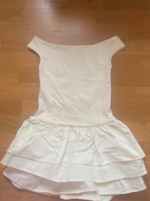 Gul volangklänning från Gina Tricot - Söt vit klänning från Gina Tricot med off shoulder-modell och dubbla volanger i kjolen. Tillverkad i mjukt tyg som ger en bekväm känsla. Perfekt för dig som gillar en enkel men ändå trendig look.