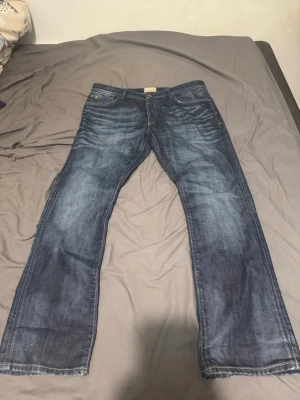 Vintage jack&jones jeans - Säljer ett par vintage jack&jones jeans med raka ben och snygga slitningar framtill. Jeansen har klassisk femficksdesign, normal midja och kontrastsömmar. Perfekta för en avslappnad och trendig look.