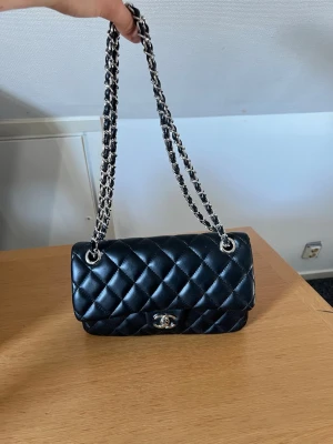 Svart quiltad handväska med kedjerem - 🚚 Fraktar direkt 📦 🚨PRIS GÅR ATT ÄNDRA 🚨Stilren svart handväska i quiltat läder med silverfärgad kedjerem och klassiskt vridlås framtill. Väskan har en elegant, rektangulär form och en liten ficka på baksidan. Perfekt accessoar för att lyfta din outfit.