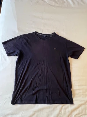 Svart basic t-shirt med liten logga - En svart basic t-shirt i mjuk bomull med rund hals och korta ärmar. Liten diskret logga på bröstet för en clean look. Perfekt till jeans eller shorts och enkel att matcha med allt.