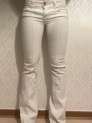 Vita bootcut jeans med pressveck - Säljer ett par vita bootcut jeans med pressveck framtill. Jeansen har låg midja, fem fickor och stängs med knapp och dragkedja. Materialet är stretchigt och ger en snygg passform. Perfekta för dig som vill ha en clean och fräsch look. Fälcken som syns på bilden vid knät typ har jag fått bort i tvätten 
