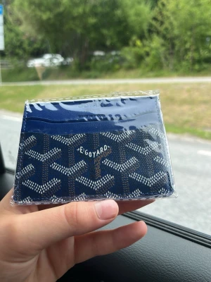 Blå mönstrad korthållare - Snygg blå korthållare med vitt och grått grafiskt mönster. Plånboken har flera kortfack och är tillverkad i ett glansigt material som ser ut som konstläder. Kommer i en grön ask med präglad logga på locket.