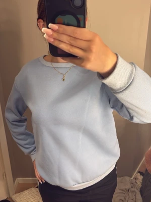 Ljusblå sweatshirt med rund hals - En stilren ljusblå sweatshirt med rund halsringning och ribbade muddar vid ärmslut och nederkant. Materialet känns mjukt och skönt mot huden.