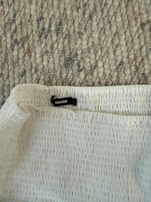 Söt kjol från bikbok  - Söt vit kortkjol från BikBok med bred smock i midjan och flera lager volanger. Kjolen har en luftig och lätt känsla, perfekt för varma dagar. Materialet känns som polyester och kjolen har en ljus ton.