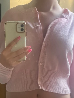 Ljusrosa cropped kofta - Söt ljusrosa cropped kofta med rund hals och långa ärmar. Koftan har ribbade muddar och knäpps med små vita knappar framtill.