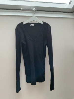 Svart långärmad v-ringad topp - En svart långärmad topp med v-ringning och figurnära passform. Perfekt basplagg att styla till olika looks. Tillverkad i ett mjukt och stretchigt material som känns skönt mot huden.