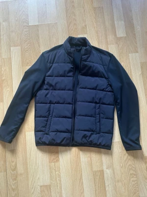 Svart jacka från Zara - Snygg svart jacka från Zara med quiltad framsida och släta ärmar. Jackan har dragkedja framtill och två fickor på sidorna. Den ser lite blå ut på bilderna pga ljuset men den är helt svart.