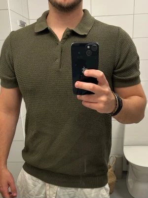 Olivgrön piké t-shirt med krage - Säljer en olivgrön piké t-shirt med klassisk krage och korta ärmar. Tröjan har en diskret struktur i tyget och ribbade muddar vid ärmslut och nederkant. Perfekt för en avslappnad men ändå stilren look.