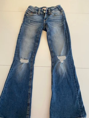 Blå bootcut jeans med slitningar - Säljer ett par blå bootcut jeans med hål på knäna och snygga broderade detaljer på bakfickorna,dom är från Gina tricot Young och är k storlek 152