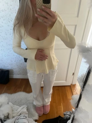 Ljusgul topp från Gina Tricot - Supersnygg ljusgul topp från Gina Tricot med lång ärm och v-ringad hals. Toppen har en figurnära passform och är tillverkad i ett mjukt, stretchigt material som känns bekvämt mot huden. Perfekt att styla med jeans eller kjol för en fräsch look.
