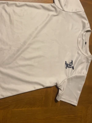 Vit t-shirt med blått mönster - Vit t-shirt i bomull med ett unikt blått mönster på bröstet och ryggen. Klassisk rund hals och korta ärmar. Perfekt för dig som gillar enkel men ändå personlig stil.