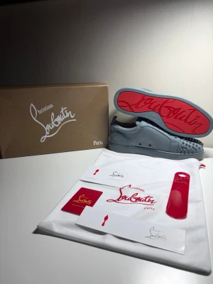 Ljusgråa Louboutin skor med spikar - Säljer ett par as feta ljusgråa/ljusblåa Louboutins med spikar i storlek 43, skorna är  helt nytt skick, aldrig använda utan bara testade. Skorna kommer med original box, skohorn, äktehetskort och allt annat som syns i bilden.