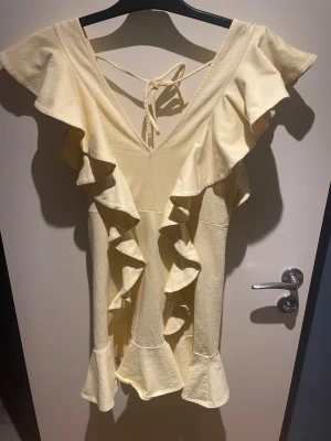 Ljusgul volangklänning med v-ringning  - Ljusgul kort volangklänning med v-ringning både fram och bak och med snörning i nacken💕