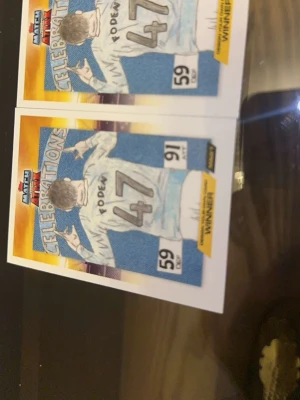 Match Attax samlarkort Foden #47 - Två Match Attax samlarkort med motiv av fotbollsspelaren Foden, nummer 47. Kortet har texten 'Celebrations' och färgerna blå, vit och gul. Siffrorna 59 och 91 syns på kortet. Perfekt för dig som samlar på fotbollskort.