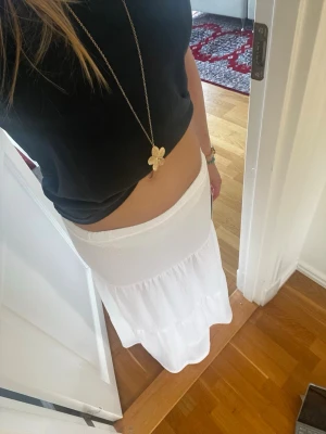 Vit långkjol med volangdetaljer - Säljer en vit långkjol med volangdetaljer och resår i midjan. Kjolen har en luftig och flowy känsla, perfekt för varma dagar. Materialet känns mjukt och lätt, troligtvis bomull eller syntet. Enkel att matcha med olika toppar för en chill look.