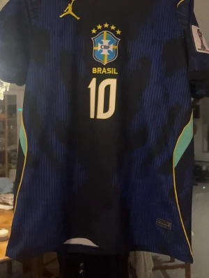 Blå Brasilien Neymar fotbollströja - Säljer en blå Brasilien fotbollströja med Neymar Jr och nummer 10 på ryggen. Tröjan har gula och ljusblå detaljer, officiellt landslagsemblem och FIFA-märke på ärmen. Perfekt för dig som älskar fotboll och vill stötta Brasilien.