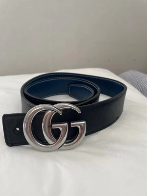 Gucci skärp herr - Snyggt svart bälte i skinn med ett stort, blankt GG-spänne i silverfärg. Perfekt accessoar för att lyfta vilken outfit som helst. Klassisk design med stilren känsla och bred rem. 