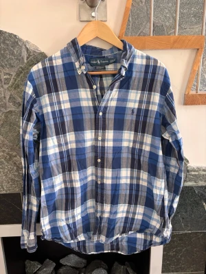 Blårutig skjorta från Ralph Lauren - Säljer en klassisk blårutig skjorta från Ralph Lauren i storlek L. Skjortan har knappar framtill, button-down krage och är tillverkad i mjuk bomull. Perfekt för dig som gillar en avslappnad men ändå stilren look.