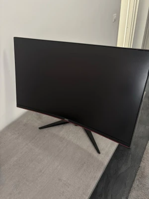 Svart datorskärm från AOC - Snygg svart datorskärm från AOC med tunn ram och röda detaljer. Skärmen har en modern, stilren design och står på ett stabilt stativ i svart plast. Perfekt för gaming eller arbete där du vill ha bra bildkvalitet och cool look.