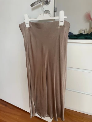 Satinkjol - Säljer en kjol i satinliknande material i brons/brun. Kjolen har en rak, figurnära passform och faller snyggt. Lite nopprig efter tvätt men går bort lätt med roller!!