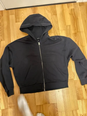 Svart hoodie med dragkedja från H&M - Säljer en svart hoodie från H&M i oversized fit. Hoodien har dragkedja framtill, två fickor och en stor huva. Tillverkad i mjukt bomullsmaterial som är skönt att ha på sig. Perfekt för en avslappnad och stilren look.