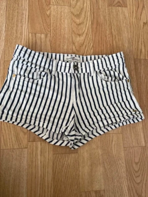 Randiga shorts från Hampton Republic - Snygga vita shorts med marinblå ränder från Hampton Republic. Klassisk femficksmodell med knappgylf och bälteshällor. Perfekta för sommardagar och har en fräsch, tidlös look.