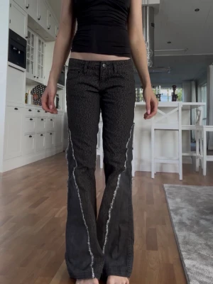Leopard bootcut jeans med kontrastsömmar - Säljer ett par svarta bootcut jeans med unika ljusa kontrastsömmar längs benen. Jeansen har låg midja, klassisk femficksmodell och ett coolt mönster i tyget. Perfekta för dig som vill sticka ut med en edgy stil.
