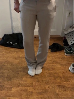 Beige kostymbyxa från BikBok - Snygga beige kostymbyxor från BikBok i rak modell. Byxorna har låg midja, pressveck och sidofickor. Perfekta för en clean och stilren look. Materialet känns mjukt och följsamt.