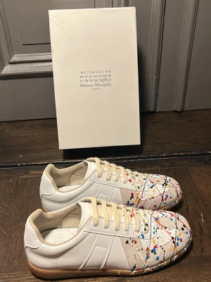Maison Margiela vita sneakers med färgstänk - Unika vita sneakers från Maison Margiela med färgstänk i rött, blått, gult och svart. Box kommer med 