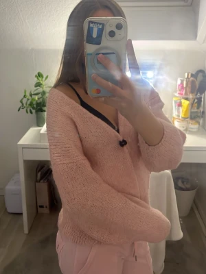 Rosa stickad cardigan - Mysig rosa stickad cardigan med öppen front och långa ärmar. Tröjan har en avslappnad passform och är gjord i ett mjukt, fluffigt material som känns skönt mot huden. Perfekt att slänga över en topp för en chill look.