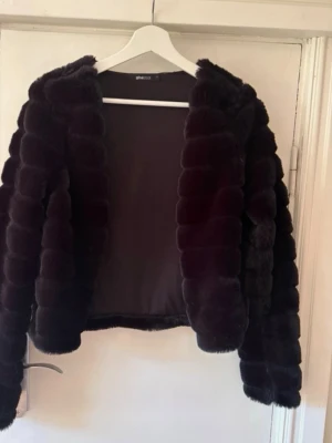 Mörklila fuskpälsjacka Gina Tricot - Säljer en fluffig mörklila fuskpälsjacka från Gina Tricot. Jackan har en kortare modell med breda, markerade pälsränder och är helfodrad. Perfekt för dig som vill ha en statementjacka med lyxig känsla och snygg struktur.
