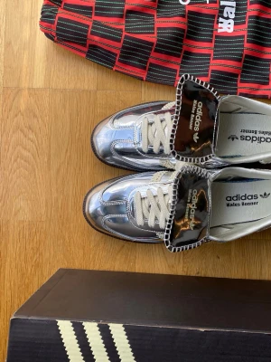 Adidas Wales Bonner silvriga sneakers - Snygga sneakers från Adidas x Wales Bonner med metallic-silverfärgad ovandel, vita snören och unika detaljer på plösen. Skorna har låg profil och klassisk retrostil, perfekt för dig som vill sticka ut med din stil.