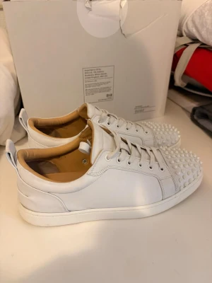 christian louboutin (Vita med spikes) - Säljer ett par vita christian louboutin läder med  nitar på tån. Skorna har en stilren design för dig  som vill sticka ut med en unik detalj på dina skor.