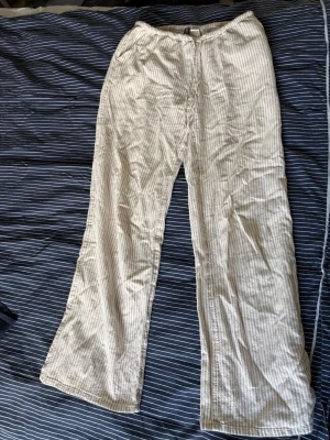 Beige- och vitrandiga linnebyxor lågmidjadd - Säljer ett par luftiga linnebyxor med beige och vita smala ränder. Byxorna har rak passform och resår i midjan för extra komfort. Perfekta för varma dagar och chill stil. Materialet är mjukt och svalt linne.
