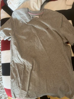 Grå t-shirt från Tommy Jeans - Snygg grå t-shirt från Tommy Jeans med liten logga på bröstet. Klassisk rund halsringning och korta ärmar. Tillverkad i mjuk bomull som känns skön mot huden. Perfekt basplagg till garderoben.