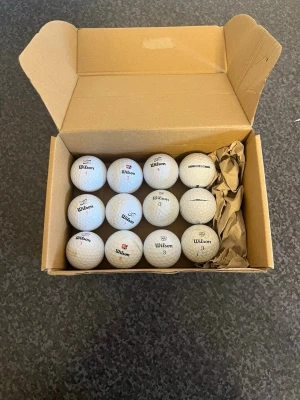 Golfbollar från Wilson i kartong - Säljer ett set med vita golfbollar från Wilson, levereras i en öppen kartong. Bollarna har klassisk dimple-yta och märkning med siffror och logga. Perfekt för dig som vill fylla på golfväskan inför säsongen.