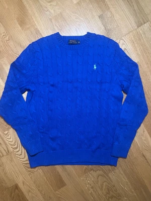 Blå kabelstickad tröja Polo Ralph Lauren - Säljer denna moderna och stilrena blåa kabelstickad tröja från Polo Ralph Lauren med rund halsringning och den klassiska broderade loggan på bröstet. Tröjan har ribbade muddar vid ärmslut och nederkant. Perfekt för dig som vill ha en stilren och tidlös look. Vid frågor, extra bilder eller liknande är det bara att kontakta mig!