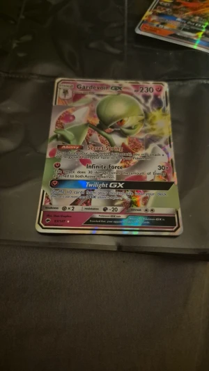 Pokémonkort Gardevoir GX holo - Säljer ett Pokémonkort med Gardevoir GX, holografisk design. Kortet har färger i grönt, rosa och gult och visar Gardevoir i en kraftfull pose. Det är ett samlarkort med attacker som Infinite Force och Twilight GX. Perfekt för samlare eller Pokémonfans.